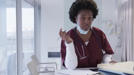 African-american-female-doctor-with-face-mask-and-taking-notes-in-hospital-room,-slow-motion