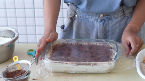 Frau,-Die-Tiramisu-Kuchen-Macht,-Verpackt-Einen-Tiramisu-Kuchen-Mit-Plastikfolie,-Bevor-Sie-Ihn-In-Den-Kühlschrank-Stellt