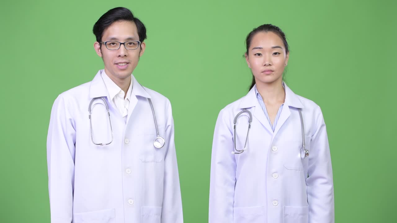 Young Asian couple doctors giving thumbs up together