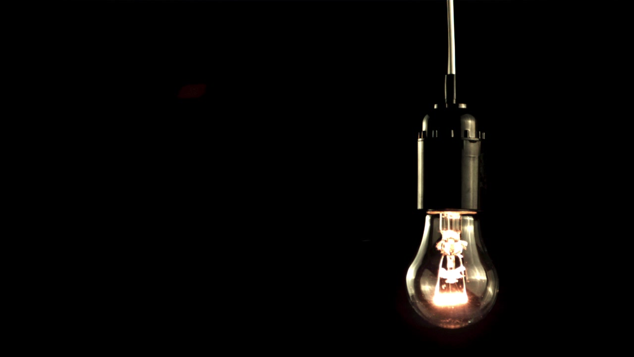 Bombilla clásica iluminándose lentamente contra un fondo negro