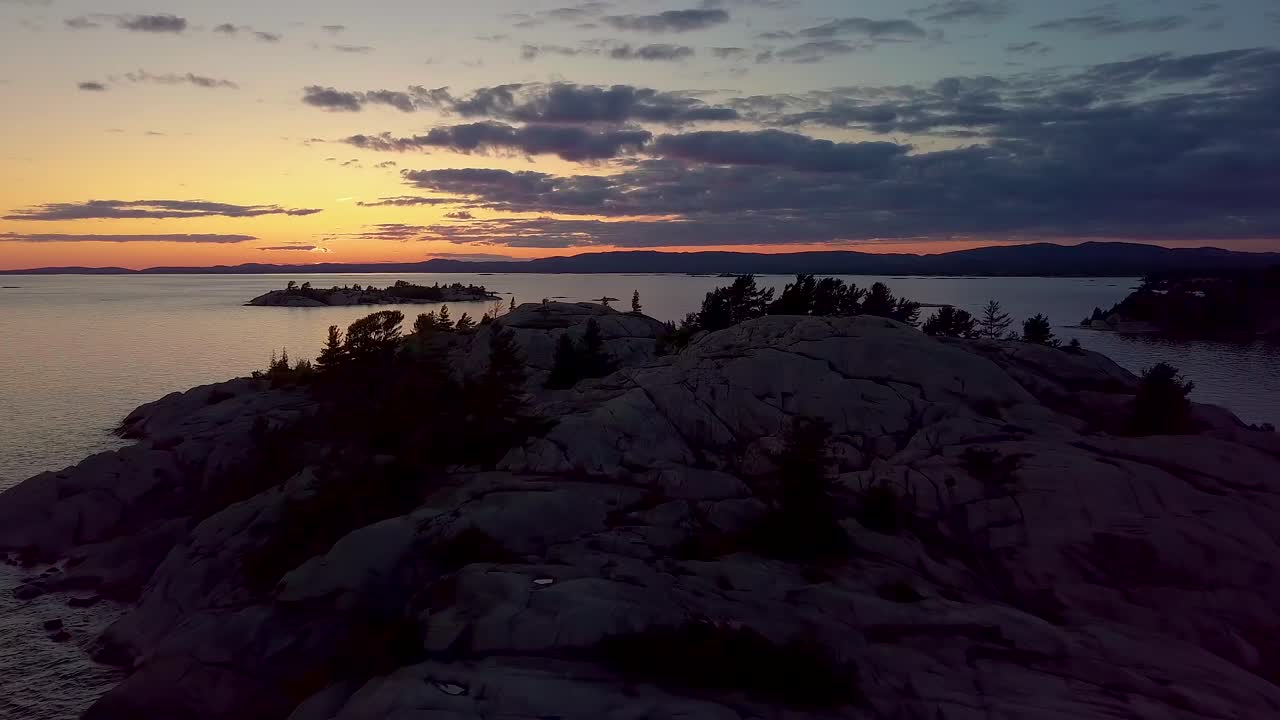 volando a baja altura sobre la isla de pinos rocosos en un gran lago justo después de la puesta del sol, una amplia plataforma aérea de drones en