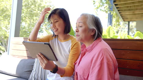 using tablet, young asian woman and senior asian woman video chatting on couch outdoors