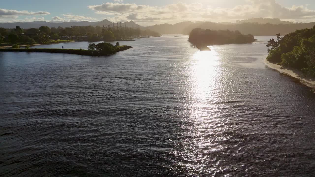 Drone captures serene sunset over Brunswick Heads river, highlighting reflective water and lush surroundings in warm, golden light