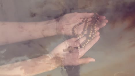 animation of caucasian woman praying with rosary over cross and clouds