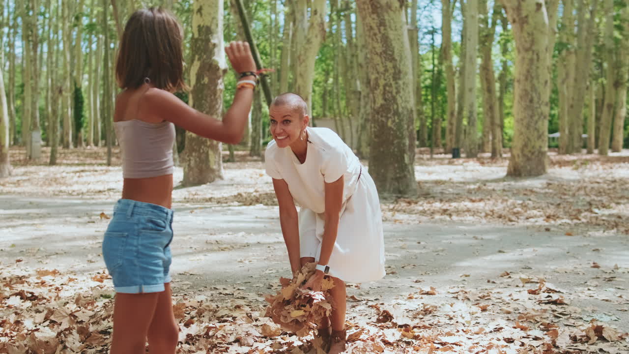 Joyful Mother and Daughter Throwing Leaves in a Forest