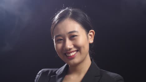 close up of smiling asian speaker woman in business suit crossing her arms while standing in the black screen studio