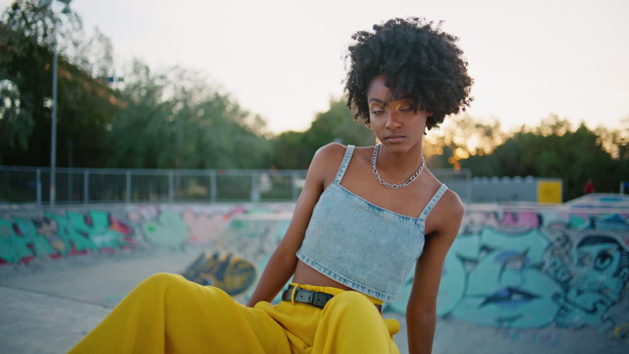 Beautiful teenager sitting skateboard looking camera close up. Curly girl skater