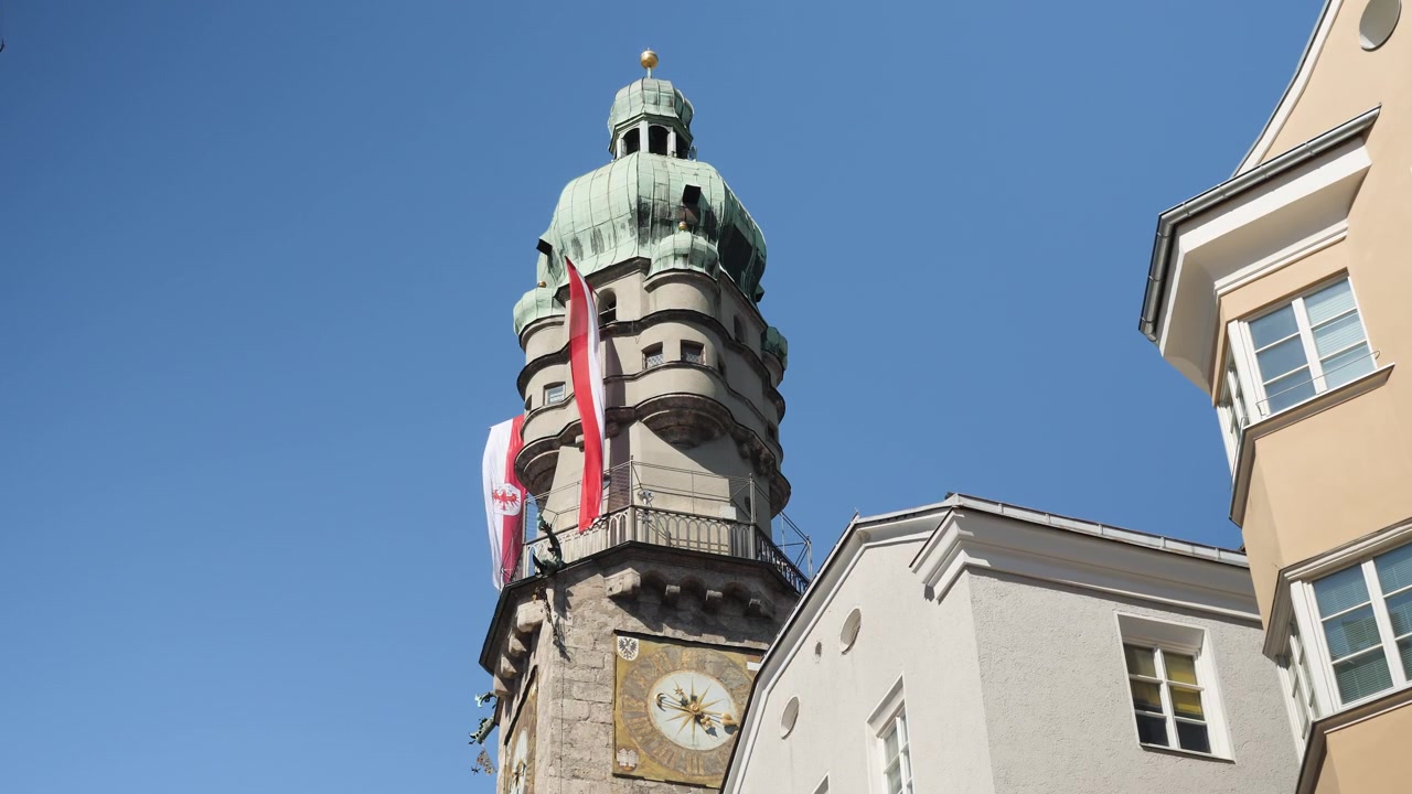 Tilt ned i skarpt middagssolskin på det historiske klokketårn og tagene i Innsbruck, Østrig, under en klar blå himmel.