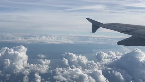 Plane-window-view-of-wing-and-beautiful-fluffy-clouds-on-sunny-day