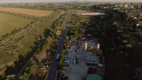 Toma-Aérea-De-Un-Camión-De-Transporte-A-Través-De-Una-Zona-Industrial,-Cerca-De-La-Ciudad-Al-Amanecer,-Revelando-La-Línea-Del-Horizonte