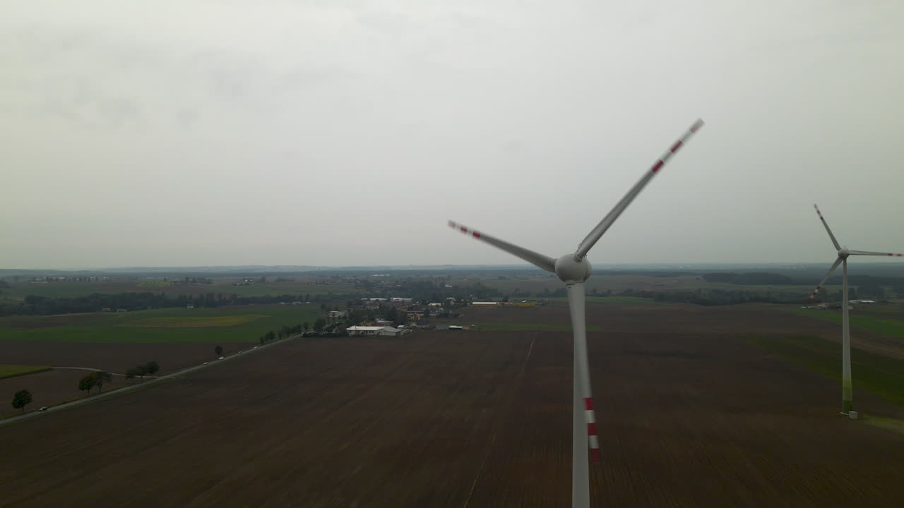폴란드의 우울한 하늘 아래 바람에 회전하는 두 개의 거대한 농장 풍차 - 드론 샷
