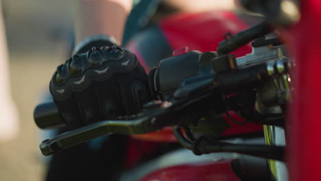 close-up of a biker s hand gripping the clutch lever while wearing protective gloves on a motorcycle, with a blurred background of something fluttering in the wind and a red bike