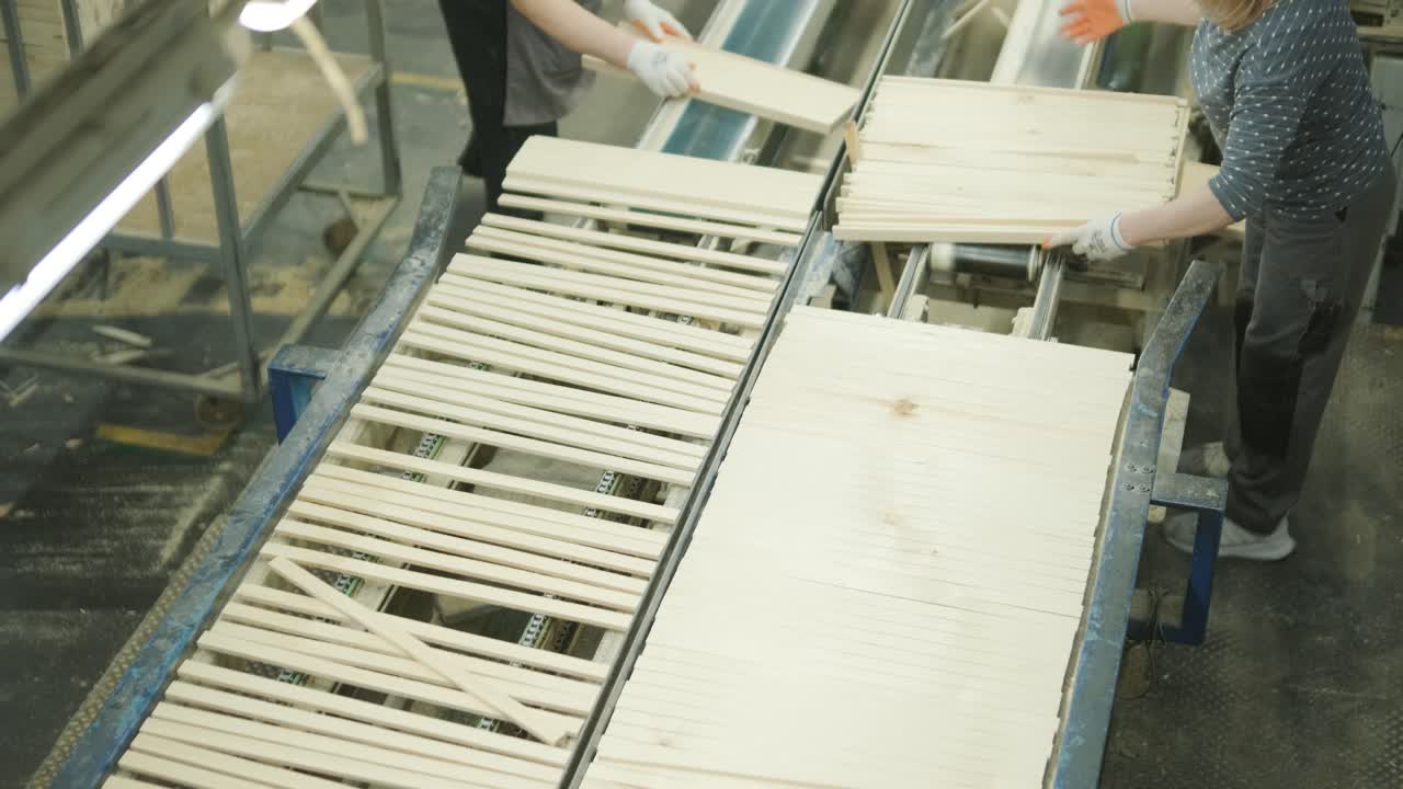 Operai che selezionano assi e listelli di legno su un nastro trasportatore in una fabbrica