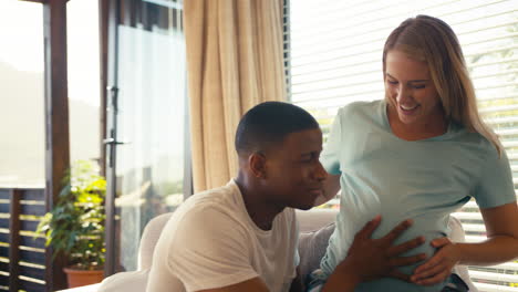 couple with pregnant woman in bedroom at home with man listening to baby's heartbeat