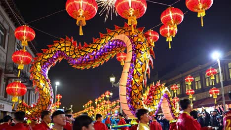 illuminated dragon puppet parading through nighttime city streets, accompanied by red lantern bearers, celebrating lunar new year's festive cultural spirit