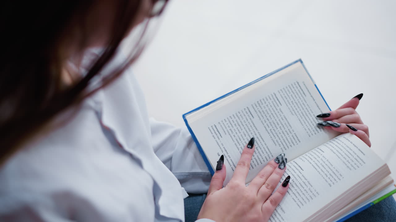 vista parcial de cerca de una mujer leyendo un libro mientras está sentada en un banco, elegantes uñas negras en contraste con páginas nítidas, luces reflectantes brillantes crean un ambiente suave