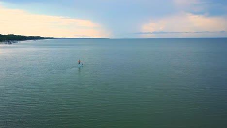 una toma dramática de un dron de un kayakista solitario deslizándose lentamente hacia una puesta de sol colorida