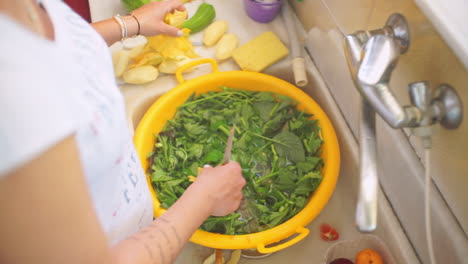 mujer lava verduras en un recipiente de plástico amarillo en casa