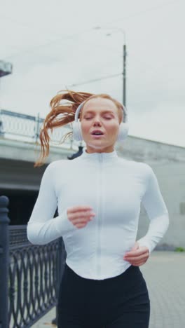 A Young Woman in Stylish Activewear Enjoys a Refreshing Run While Listening to Music on Headphones, Exuding Energy and Motivation in an Urban Setting
