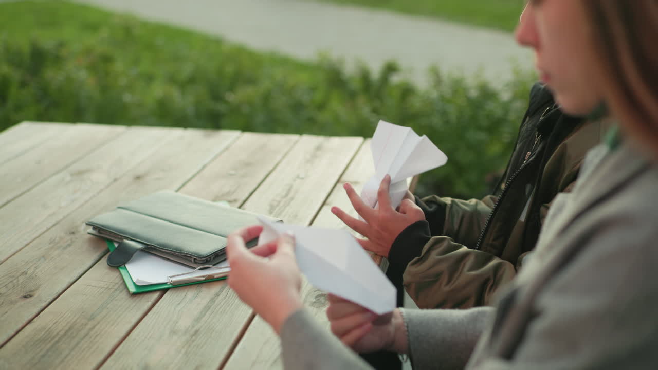 Primo piano da dietro di persona che tiene in mano un aquilone di carta piegato mentre è seduta a un tavolo di legno all'aperto, che mostra un'attività di creazione creativa con un'atmosfera informale e un focus sul design fatto a mano
