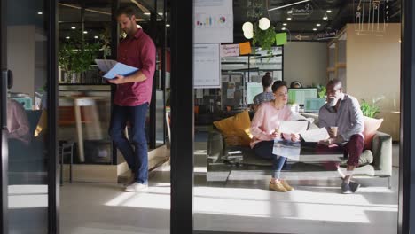 Diverse-business-people-sitting-with-documents-and-discussing-work-at-office