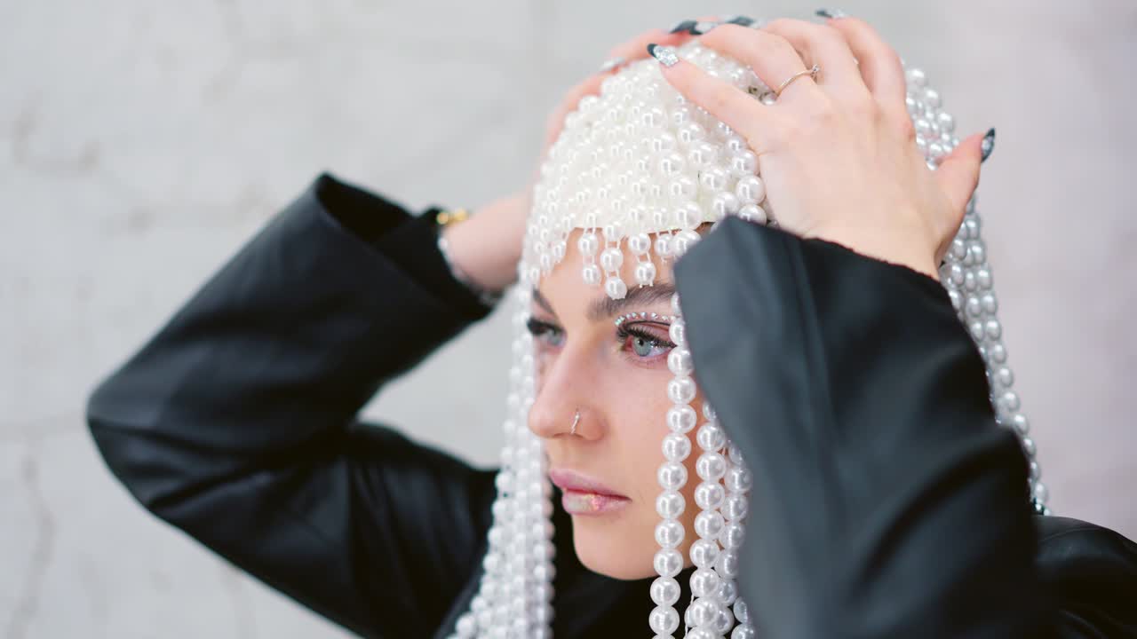 Close-up portrait of a woman wearing an elaborate pearl headpiece and artistic eye makeup