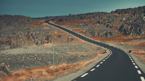 a narrow asphalt road leading through the desolate tundra landscape