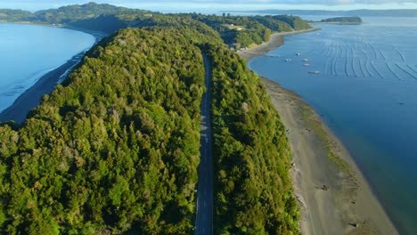 aerial shot of a car driving along a narrow channel on lemuy island, chiloe, lush scenery