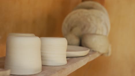 handmade pots and plates lying on shelf in pottery workshop