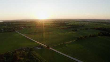 Luftdrohne-Schoss-über-Ländliche-Landschaft-Mit-Straßen,-Die-Von-Grünen-Wiesen-Auf-Beiden-Seiten-In-Wisconsin,-USA,-Umgeben-Sind,-Mit-Sonnenaufgang-über-Dem-Horizont