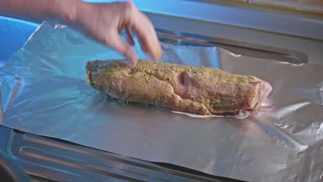 a chef's white hand places a tender marinated pork tenderloin onto foil on a kitchen countertop