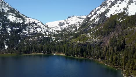 Vista-Aérea-Del-Agua-Alpina-En-El-Lago-Tahoe-Y-La-Costa-Bajo-Los-Picos-Nevados-De-Sierra-Nevada-En-El-Parque-Estatal-Emerald-Bay-Ee.uu.