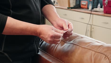 worker readies sandpaper over brown leather sofa surface before gentle sanding