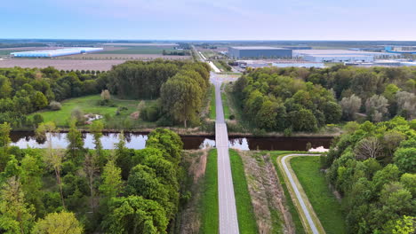 road leading to the bridge crossing the narrow river. aerial perspective on the green countryside of the netherlands. industrial premises at backdrop.
