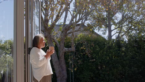 senior woman enjoying morning coffee while standing outside in garden, copy space