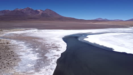 Aerial-descend-pan-across-blue-river-with-white-salt-flats-in-Bolivia