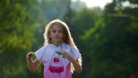 small cute girl with blond curly hair jumps happily in summer park. happy kid`s emotions outside. long hair of sweet girl.