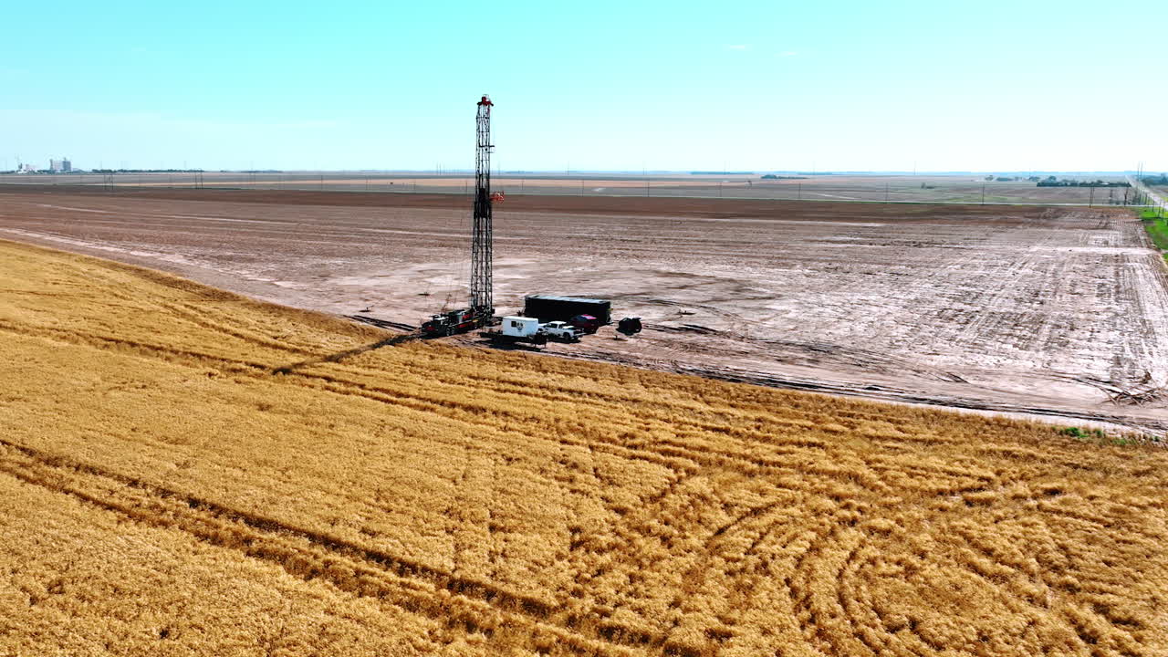 Flying above the ripe golden wheat field to approach the oil rig. Truck with tower for boring natural resources is surrounded by other cars.