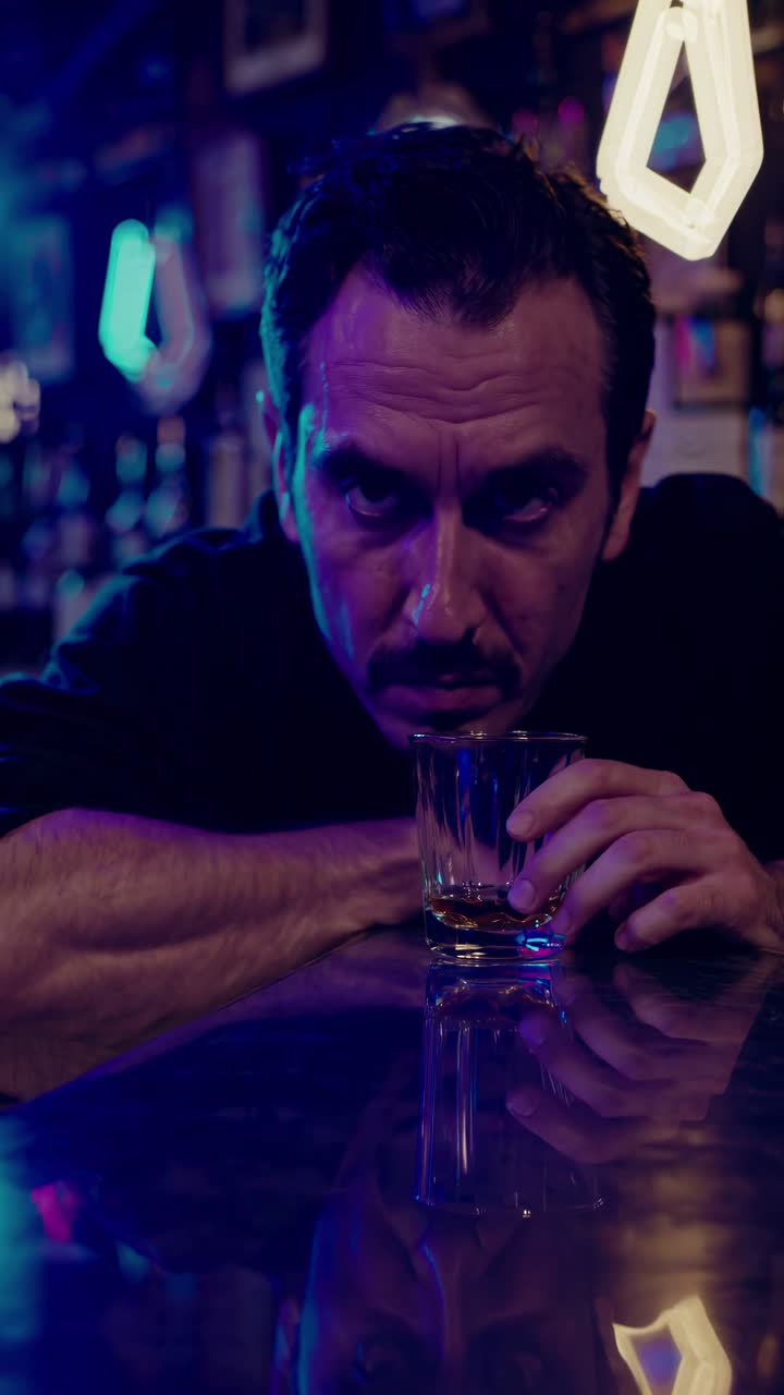 Stemningsfull barscene med en mann som holder en drink, fanget i et nærbilde, filmet fra lav vinkel.