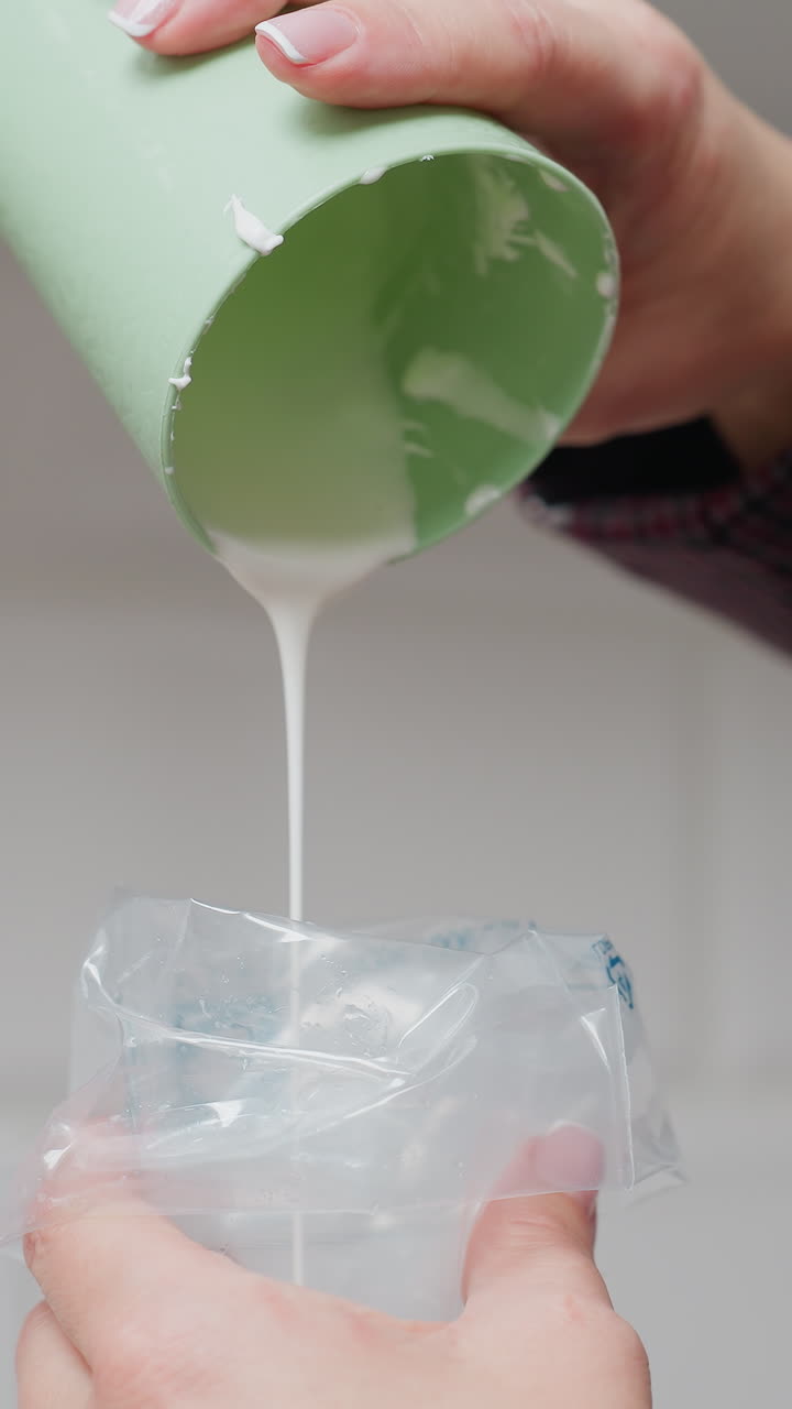 primer plano de una mujer convirtiendo el yogur cremoso en una textura parecida al cuero en la cocina, vertiendo cuidadosamente de una taza verde en una bolsa de tubería, preparando para el postre, hornear o decoración culinaria