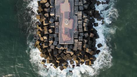 waves crash against a modern coastal promenade built with giant cubed shaped concrete blocks for tourist to use