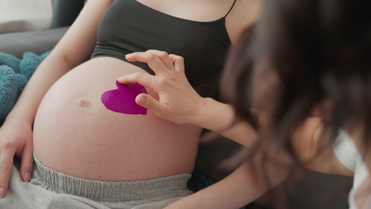 Una mano che dipinge un cuore viola sulla pancia di una donna incinta