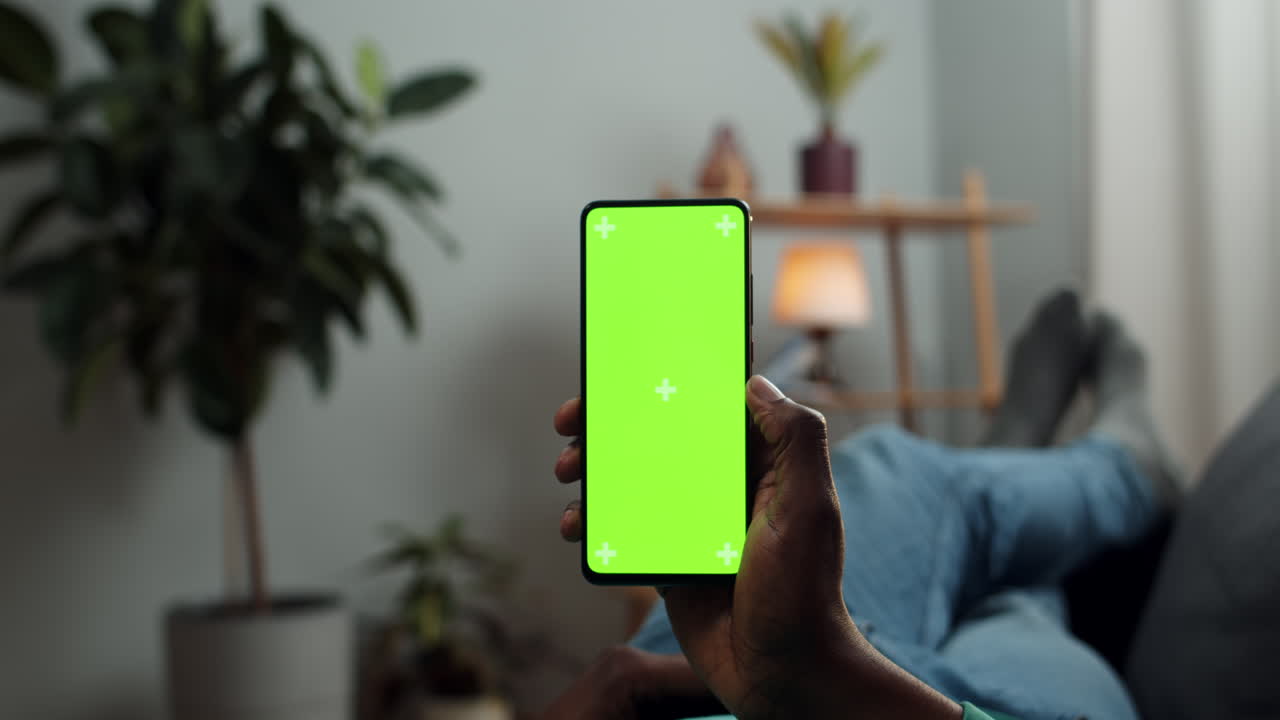 Person holding smartphone with green screen indoors