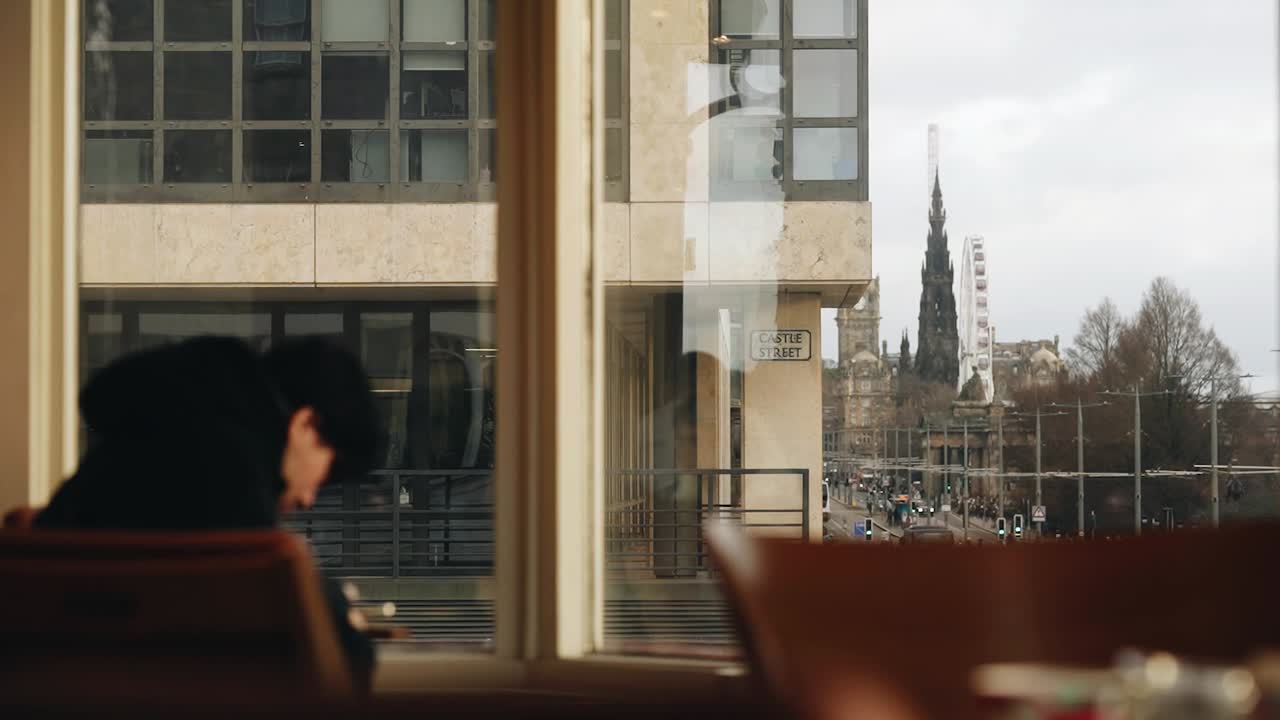 Dynamic urban café scene in Ho Chi Minh City, showing a lone person engrossed in work. Bright city skyline visible through large windows. Calm mood, soft daylight, modern vibe
