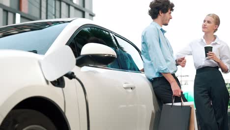 hombre de negocios y mujer de negocios progresistas apoyándose en el coche y el punto de carga.