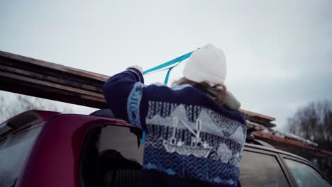 View-Behind-Man-Tying-Pieces-Of-Lumber-On-Roof-Rack-Of-SUV-Car-In-Winter