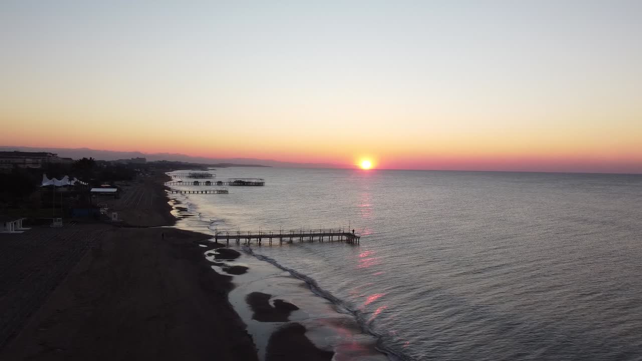 Man on an old pier, sun is rising up on horizon, wavy sea drone shot