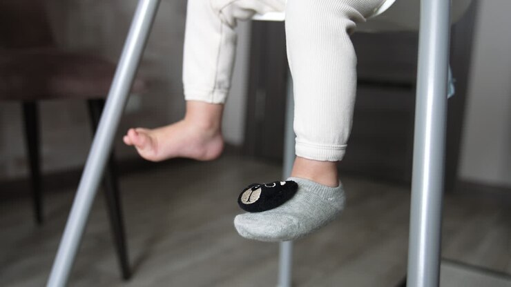 Adorable feet of a little baby sitting on the chair. One foot is bare and the other is in sock with teddy bear face on. Close up.