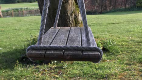 LOCKED-OFF-side-view-of-wooden-swing-seat-gently-swaying-in-the-wind