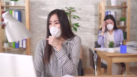 two sick young asian office workers in protective medical masks on their faces work in the office